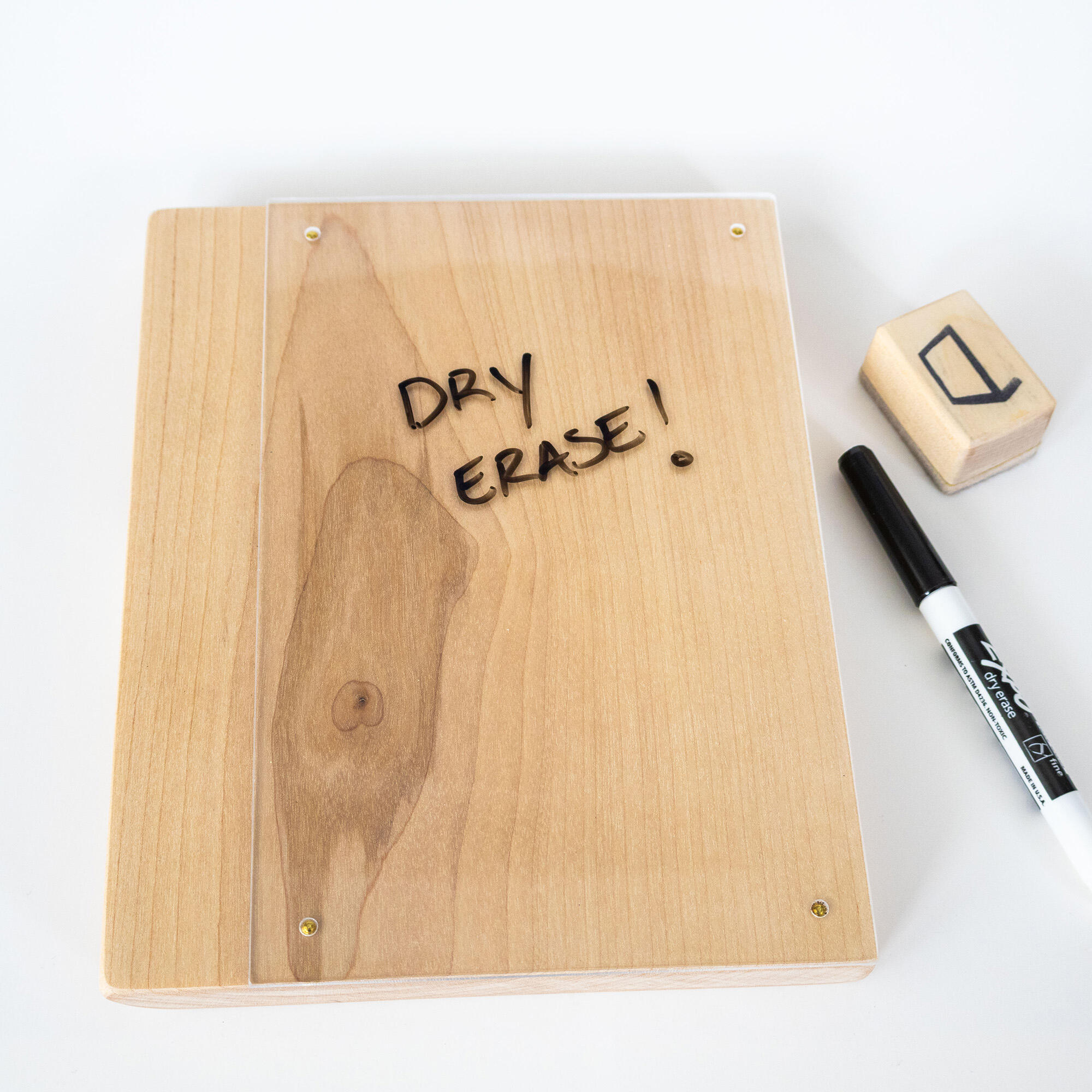 Minimalist wooden dry‑erase board with clear acrylic surface and brass corner nails, shown with a black marker and wooden eraser.