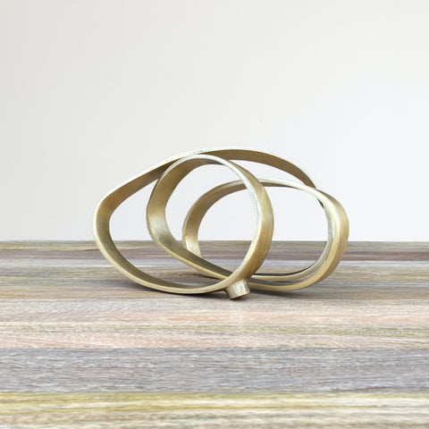 Iron sculpture in gold finish, resembling ribbon intertwined into 3 circles.