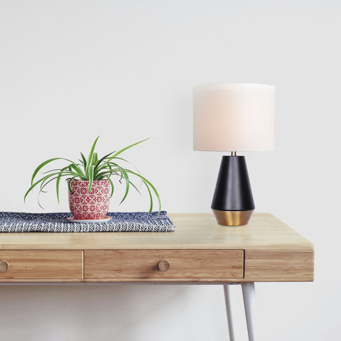 geometric modern table lamp in setting on a wooden table next to a plant. White wall mid-day.