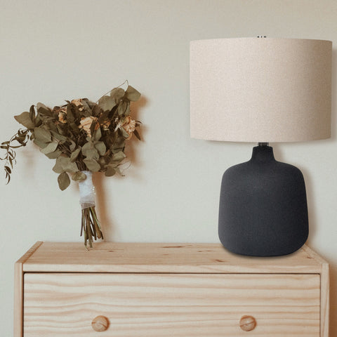 Ceramic Table Lamp with beige drum shade, and black vase-shaped base on a dresser next to a plant