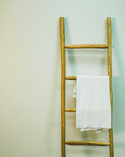 Decorative rustic ladder in natural eucalyptus wood with a towel hanging on one rung.