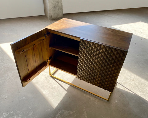 Dark brown mango wood sideboard with a CNC carved repeating pyramid pattern on the two doors. Brass finished iron legs & frame. One door open.