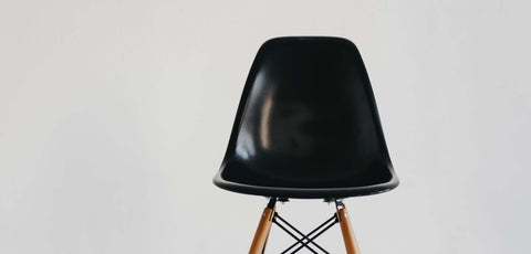 Black fiberglass Scandinavian style chair on light grey background.