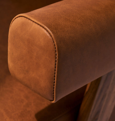 Caramel brown leather lounge chair with leather armrests and solid ash wood legs stained walnut. Front armrest detail.