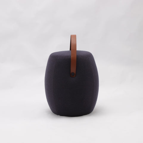 Portable dark grey cashmere pouf / stool with a brown synthetic leather strap handle.